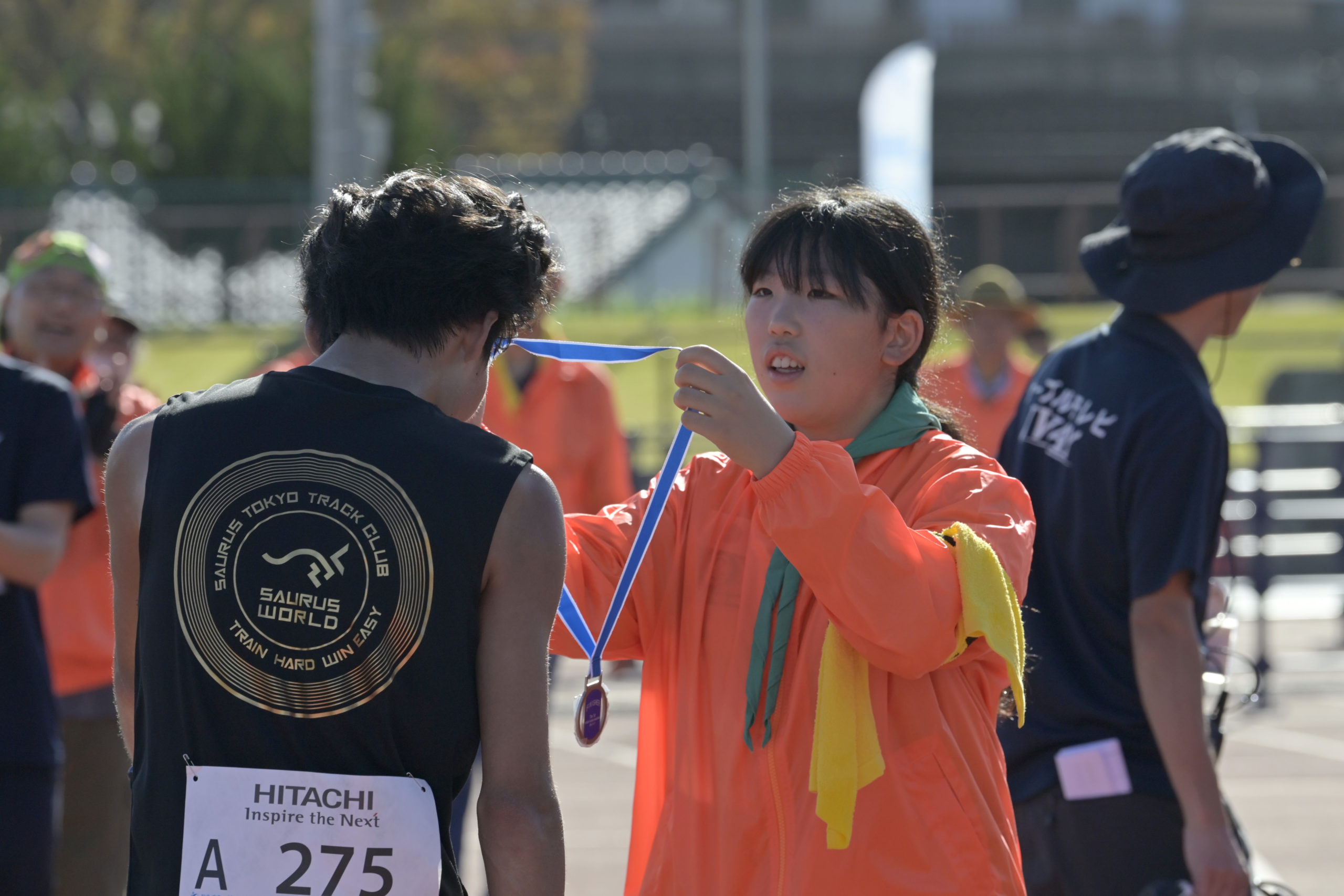 完走メダルをゴールしたランナーの首にかけるボランティア＝日立市民運動公園陸上競技場