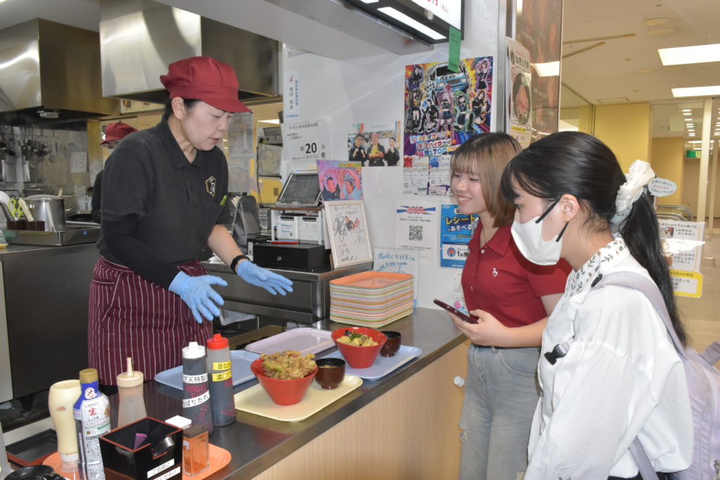 飲食店などのマップ作りのため取材する学生たち(右)=日立市幸町